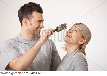 Young couple having fun at painting house, man trying to paint girlfriend nose.
