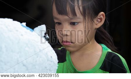 A Little Girl Paints With A Brush On The Figure Of A White Pig-shaped Papier-mache At Home. Make You