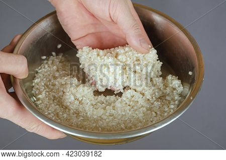 A Man Washes Raw White Rice In Fresh Water. Hands Stirring Grains Of Uncooked Wet Rice In A Metal Bo