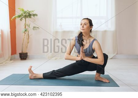 A Woman In Sweatpants And A Crop Top Practicing Yoga Performs A Skandasana Exercise With Namaste On 