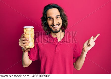 Young hispanic man holding bottle with boiled potatoes smiling happy pointing with hand and finger to the side 