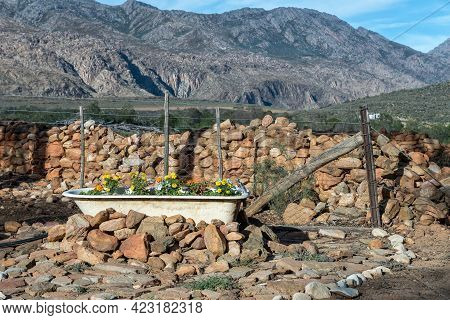 A Bathtub, Used To Plant Flowers In, A Fence And A Sandstone Wall At The Foot Of The Swartberg Mount