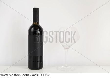 Black Bottle Of Red Wine On A White Background With Copy Space. Wine Mockup On The Table With A Glas