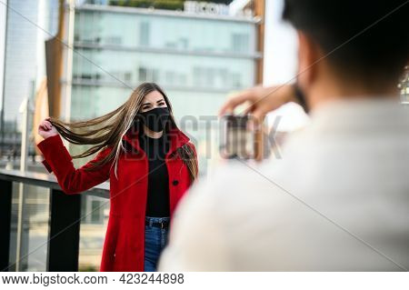 Man taking pictures of hif girlfriend outdoor wearing protective mask against covid coronavirus pandemic