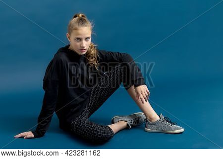 Teen Girl In Black Hoodie Sitting On Floor. Portrait Of Beautiful Serious Teenager Dressed Black Swe