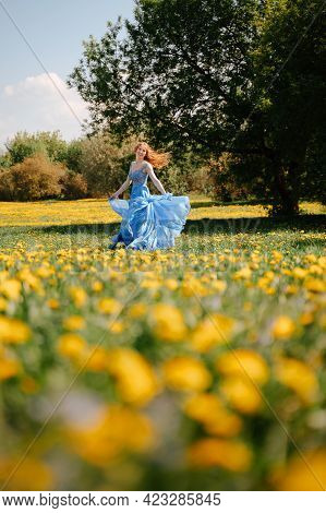 A Happy Fairy-tale Girl In An Airy Blue Dress Runs Joyfully Along The Green Lawn In The Park. Bloomi