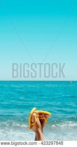 feet of a young man, upside-down on the beach, wearing a pair of yellow flip-flops, against the sky with a blank space on top, in a vertical format to use for mobile stories or as smartphone wallpaper
