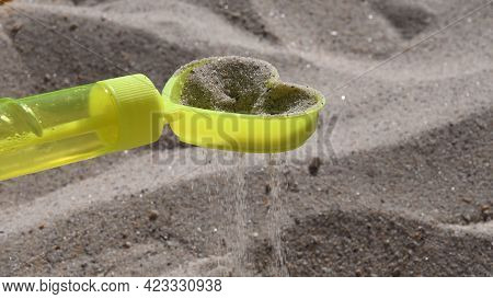 Sand Grains Pouring Through Sand Sifter. Yellow Plastic Toy Sand Sifter In Shape Of Heart. Games Wit