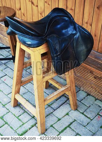 Wooden Bar Stool With A Decorative Leather Saddle On The Seat Stands On The Paving Slabs Near The Wo