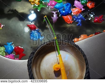 A Toy Fishing Rod Hangs Over A Miniature Pool With Plastic Colorful Fish. Child Game