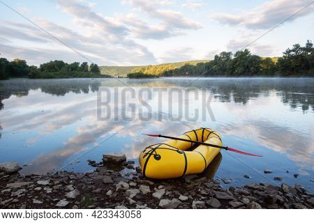 Yellow packraft rubber boat with red padle on a sunrise river. Packrafting. Active lifestile concept