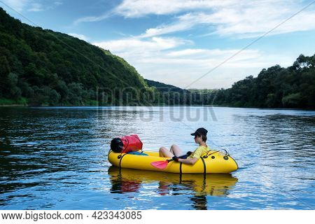 Tourist on yellow packraft rubber boat with red padle on a sunrise river. Packrafting. Active lifestile concept