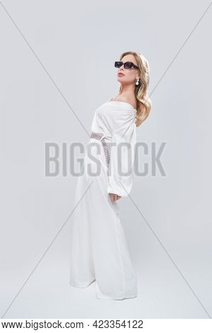 Luxury lifestyle. Full length portrait of a glamorous middle-aged woman in a chic suit and jewelry posing at studio on a white background. Fashion shot. 
