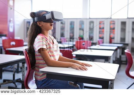 African american girl wearing vr headset while sitting on her desk in the class at school. school and education concept