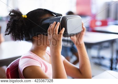 African american girl wearing vr headset while sitting on her desk in the class at school. school and education concept