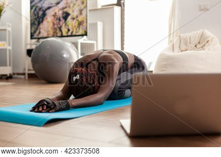Black Woman Exercising And Stretching Her Body Doing Flexibility Exercises Sitting On Yoga Mat In Ho