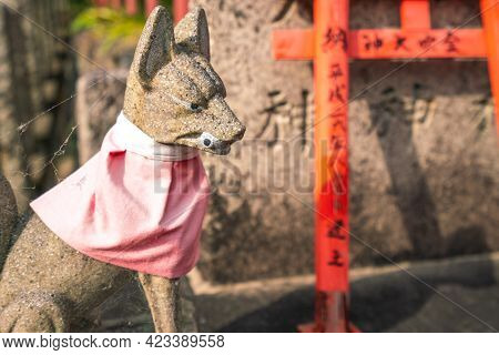 Kyoto, Japan - 05.19.2019: A Stone Statue Of Dog With Eyeball In Its Mouth With A Pink Neck Scarf On