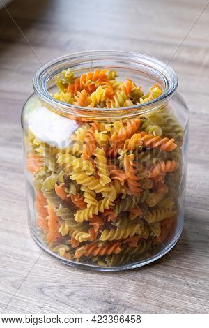 A Portrait Of A Glass Pot, Jar Or Bowl Full Of Spirelli In Three Different Colors. The Uncooked Tric