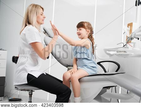 Cute Little Girl And Female Dentist Giving High Five After Dental Procedure. Smiling Child Sitting O