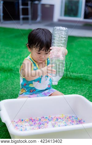 Vertical Image. Asian Baby Boy Playing Colorful Water Beads. Child Pouring Rainbow Beads From Bottle