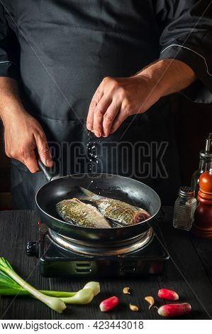 Chef Prepares Fresh Fish In Pan Sprinkling Salt With The Ingredients. Preparing To Cook Fish Food. W