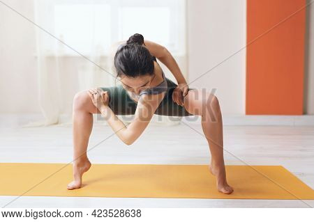 A Woman In Shorts And A T-shirt, Practicing Yoga, Performs A Twisting In Rudrasana While Standing On