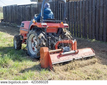 The Man Sits In A Small Tractor And Drives Through The Field Mulching Grass. Land Cultivation, Agrot