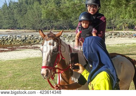 Labuan,malaysia-sept 1,2019:young Smiling Woman Mother And Small Daughter Sitting On Horse And Ridin