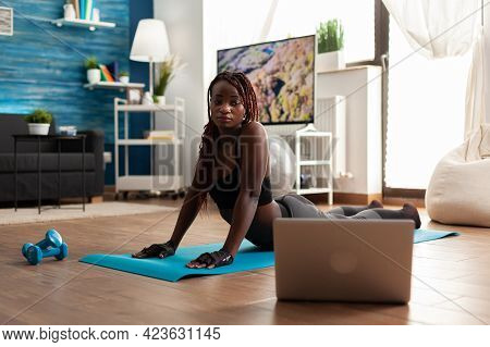Black Woman Exercising And Stretching Her Body Doing Flexibility Exercises Sitting On Yoga Mat In Ho