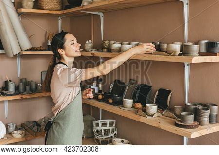 Young Woman Arranging Goods In Pottery Workshop. Creative People And Hobby Concept.