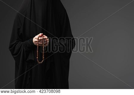 Partial View Of Muslim Nun In Black Abaya Holding Praying Beads Isolated On Dark Grey