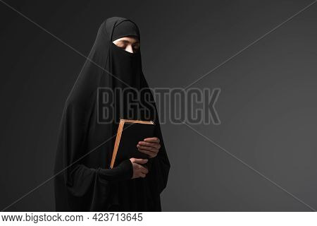 Young Muslim Nun Holding Koran While Praying With Closed Eyes Isolated On Black