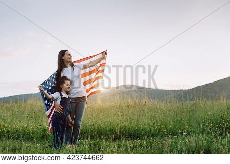 Cute Young Mother And Sweet Small Daughter Holds Usa United States Flag Standing On Green Meadow At 