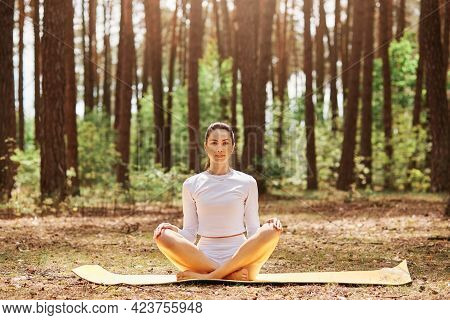 Young Beautiful Woman With Pleasant Appearance Sitting On Karemat In Yoga Pose And Looking Directly 