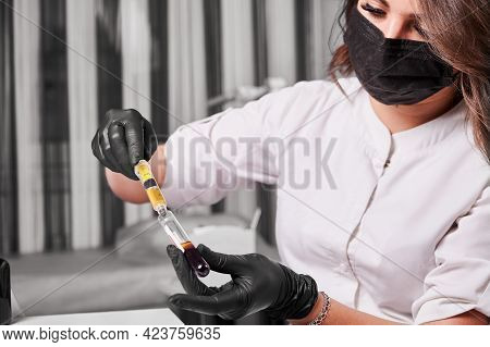 Close Up Of Young Woman Scientist In Medical Mask Holding Test Tube With Blood Sample. Female Techni