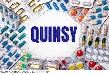 The Word Quinsy Is Written On A Light Background Surrounded By Multi-colored Packages With Pills. Me