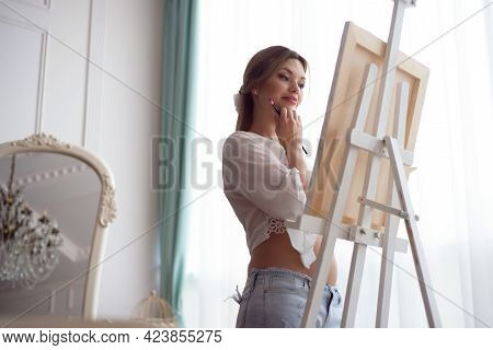 Portrait Of A Young Pragnant Woman Painting With Oil Paints On White Canvas, Side View Portrait