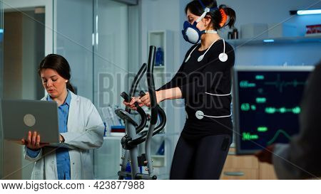 Medical Researcher Using Laptop While Measuring Sportsman Endurance Using Body Sensors, Electrodes A
