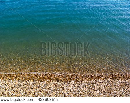 A View Of A Sunny Beach With A Town Line, A Few Beachgoers And A Calm Emerald Sea