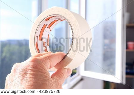 The Concept Of Self-repair. A Woman's Hand Holds A Masking Tape On The Background Of An Open Balcony