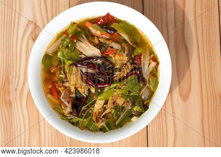 Sour And Spicy Smoked Dry Fish Soup In A White Ceramic Plate On A Wooden Table . Tom Klong In Thai. 