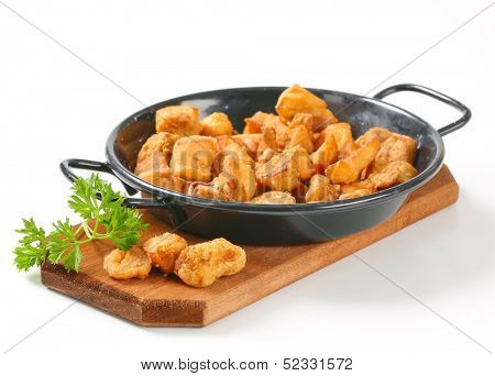 portion of fried greaves in a iron pan with cutting board