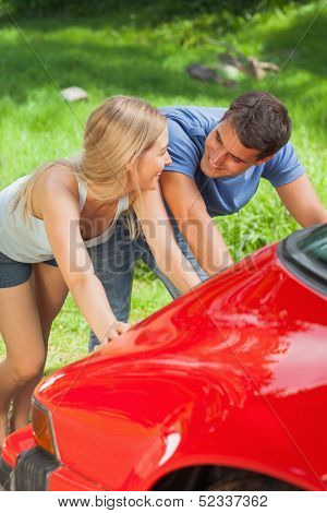 Happy couple pushing their broken down car together