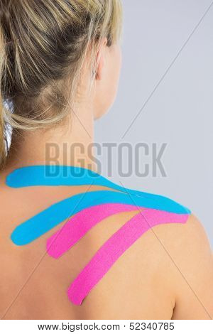 Close up of patients shoulder with applied pink and blue kinesio tape in bright office
