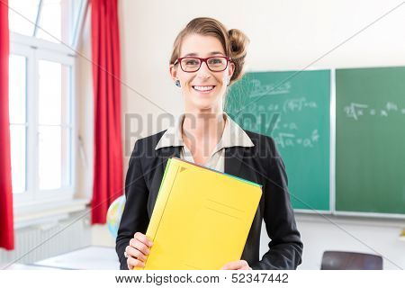 Teacher or docent in school holding folder in her hands in front of a blackboard in school class