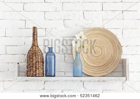 Decorative shelf on white brick wall with vintage bottles and wicker jars on it