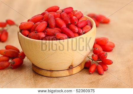 ripe barberries in wooden bowl, on wooden background