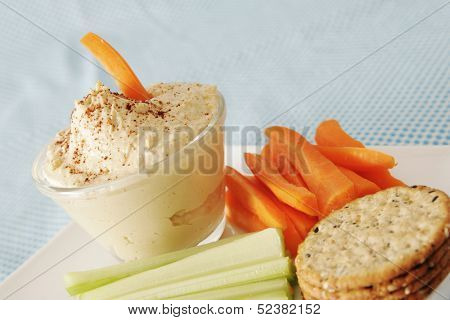Hummus in a clear bowl with carrot and celery in a white plate