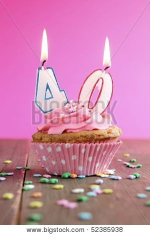 Number forty birthday candles on a pink cupcake on a wooden table