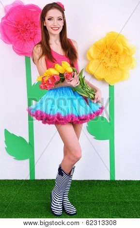 Beautiful young woman in petty skirt with bouquet of tulips on decorative background
